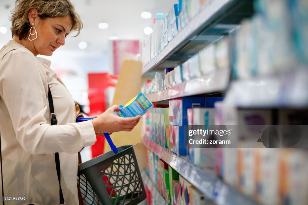 Donna che guarda il pacchetto di assorbenti e sceglie il prodotto giusto al supermercato