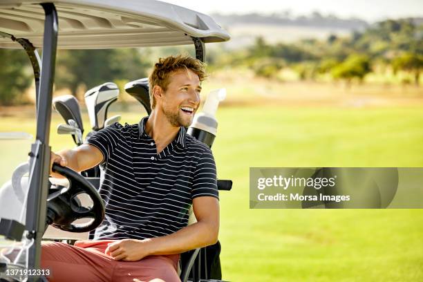 happy golfer riding in golf cart at field - golfing stockfoto's en -beelden