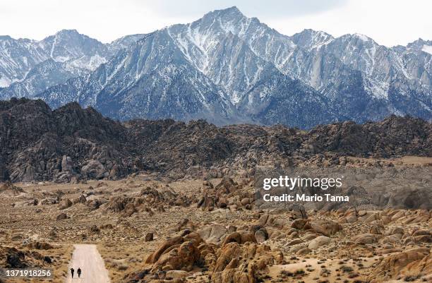 Film crew workers walk through the Alabama Hills beneath the lightly snow-capped Sierra Nevada Mountains on February 20, 2022 near Lone Pine,...