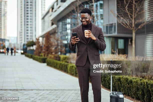 smiling businessman with smart phone and cup - black suit stockfoto's en -beelden