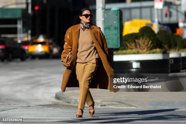 Guest wears black sunglasses, a brown / white / orange print pattern silk scarf, a brown wool pullover, a camel shiny leather with sheep interior...