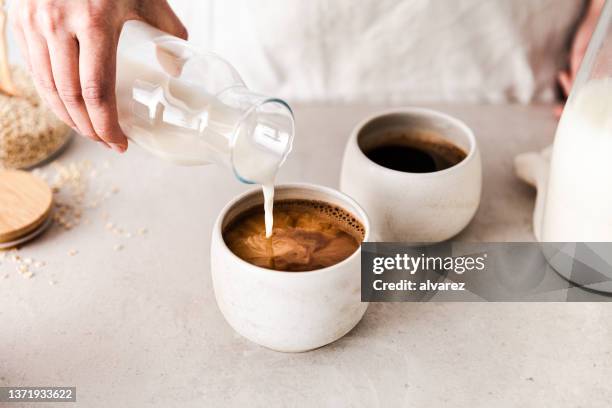 close-up of pouring oat milk into a black coffee c - koffie stockfoto's en -beelden