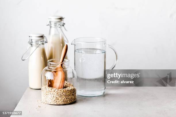 flaschen hafermilch mit wasserkrug und haferglas auf dem tisch. - haferflocken stock-fotos und bilder