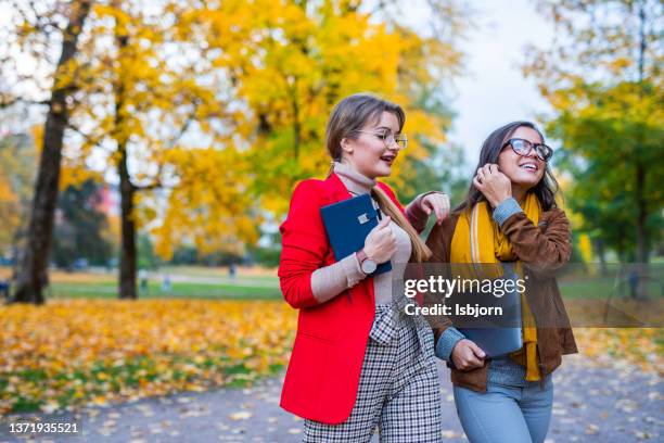 two young female coworker walking in autumn park - leesbril stockfoto's en -beelden