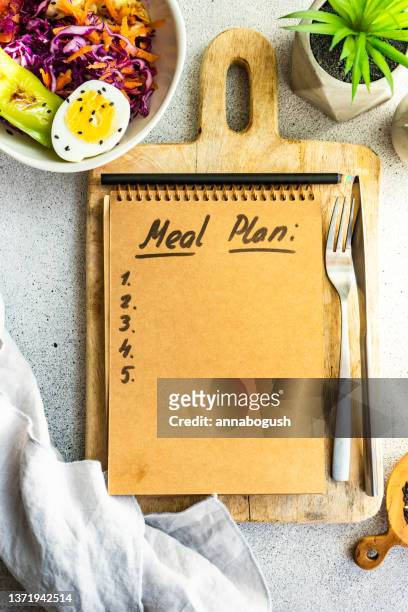 overhead view of a bowl of red cabbage, carrot, green pepper and boiled egg salad and notepad with a meal plan list - meal plan stock-fotos und bilder