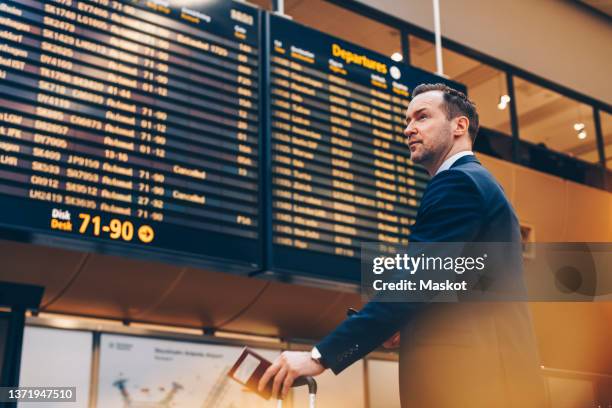 businessman looking at arrival departure board in airport - airport departure board stock pictures, royalty-free photos & images