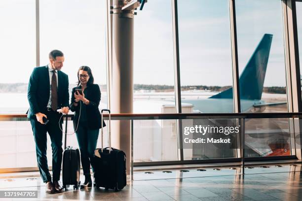 full length of business couple with luggage using mobile phone in airport - business trip stock-fotos und bilder