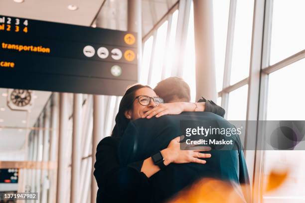 smiling businesswoman embracing businessman at airport terminal - flughafen stock-fotos und bilder