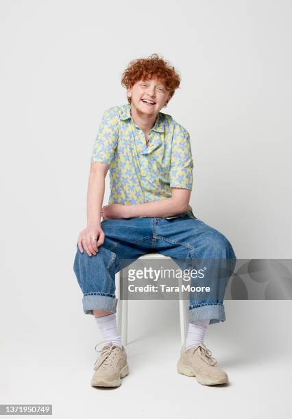 transsexual male smiling at camera and sitting on stool - portrait man studio foto e immagini stock