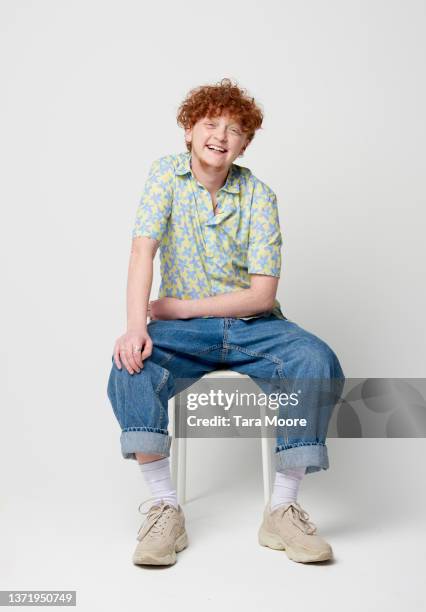 transsexual male smiling at camera and sitting on stool - jeans stock pictures, royalty-free photos & images