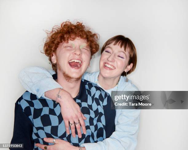 young non binary person and transsexual male hugging and laughing against white background - nb stock pictures, royalty-free photos & images