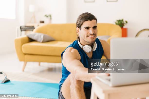 young athletic instructor man preparing an online fitness class on his laptop at home. - train spain stockfoto's en -beelden