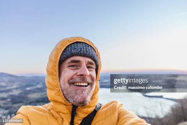 hiker with hooded down jacket in mountain taking a selfie smiling - photographing self stock pictures, royalty-free photos & images