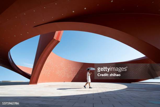 someone holding an umbrella in red curved abstract architectural space - chapéu vermelho imagens e fotografias de stock