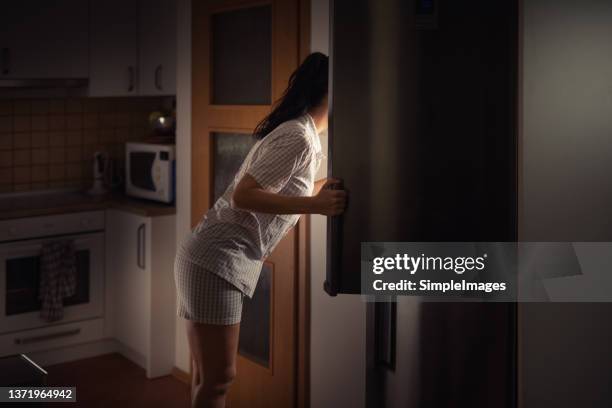 woman leaning into fridge at night searching for food with bad diet habits. - an evening with the women of homeland stockfoto's en -beelden