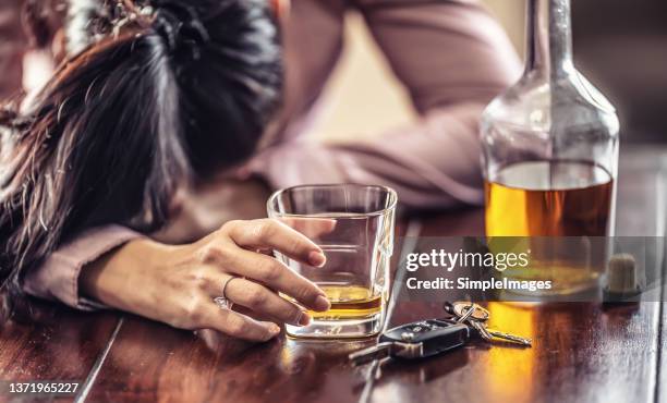 excessively alcohol drinking woman falls asleep on a table still holding glass of whisky next to car keys. - alcolismo foto e immagini stock