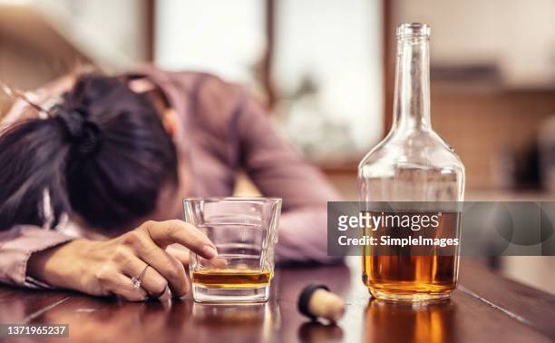 woman drinking schnaps lies with her head on the table with bottle half empty and a glass in her hand. - alcoholic stock-fotos und bilder