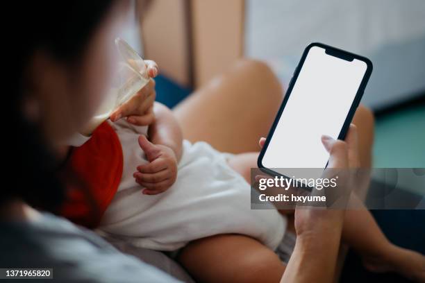 mother holding hand of her baby and touching smartphone screen - boy looking over shoulder stock pictures, royalty-free photos & images