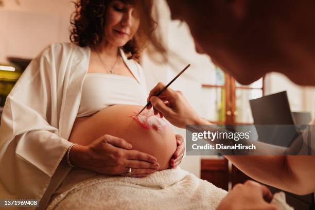 father-to-be painting the pregnant belly of his beloved wife - body art stock pictures, royalty-free photos & images