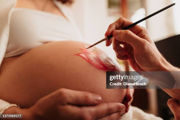 intimate close up of the father-to-be painting the pregnant belly of his beloved wife. - body art stockfoto's en -beelden