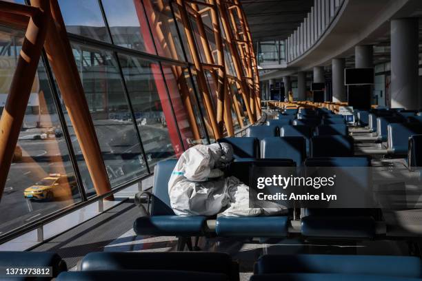 An airport staff member in a hazmat suit checks her phone at the Beijing Capital International Airport on February 21, 2022 in Beijing, China....