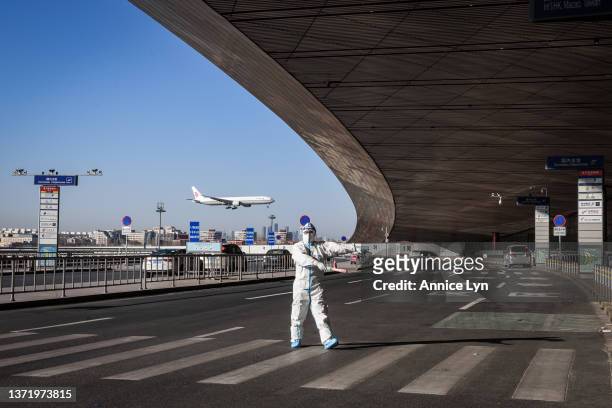 An airport staff member in a hazmat suit monitors traffic outside the entrance of the Beijing Capital International Airport on February 21, 2022 in...