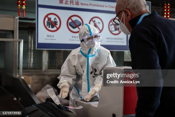 An airport staff member in a hazmat suits helps a member of the media check in for his flight at the Beijing Capital International Airport on...