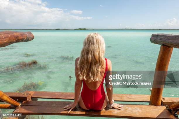 young woman on a treehouse above a beautiful lagoon, sunny day - red swimwear stock pictures, royalty-free photos & images