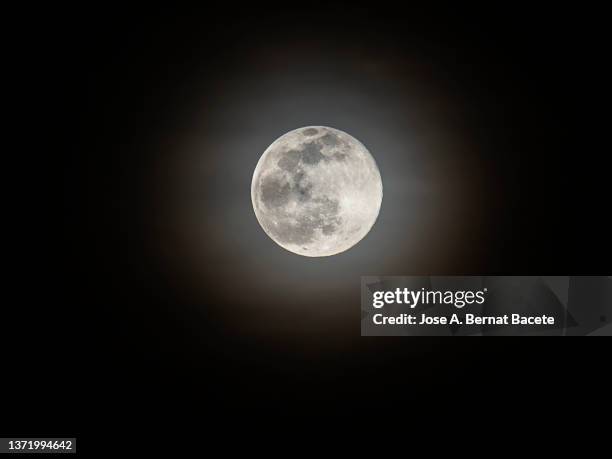 full frame of the full moon with a halo of glow over thin clouds. - planetary moon stockfoto's en -beelden