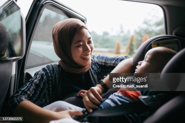 donna musulmana asiatica che allaccia il suo seggiolino per bambini - asian baby foto e immagini stock