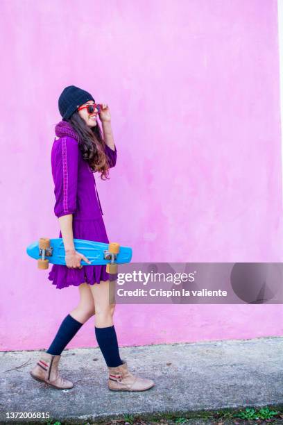 young woman in purple dress with small blue skateboard in the city - woman wearing purple dress stock pictures, royalty-free photos & images