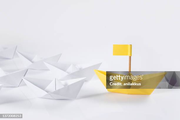 führungskonzepte mit yellow paper boat führend unter weißen booten - paper boat stock-fotos und bilder