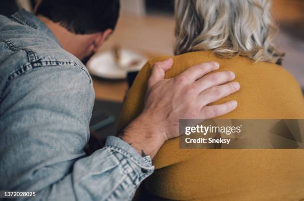 son hugging his mother while sitting on the couch. - shoulder stock pictures, royalty-free photos & images