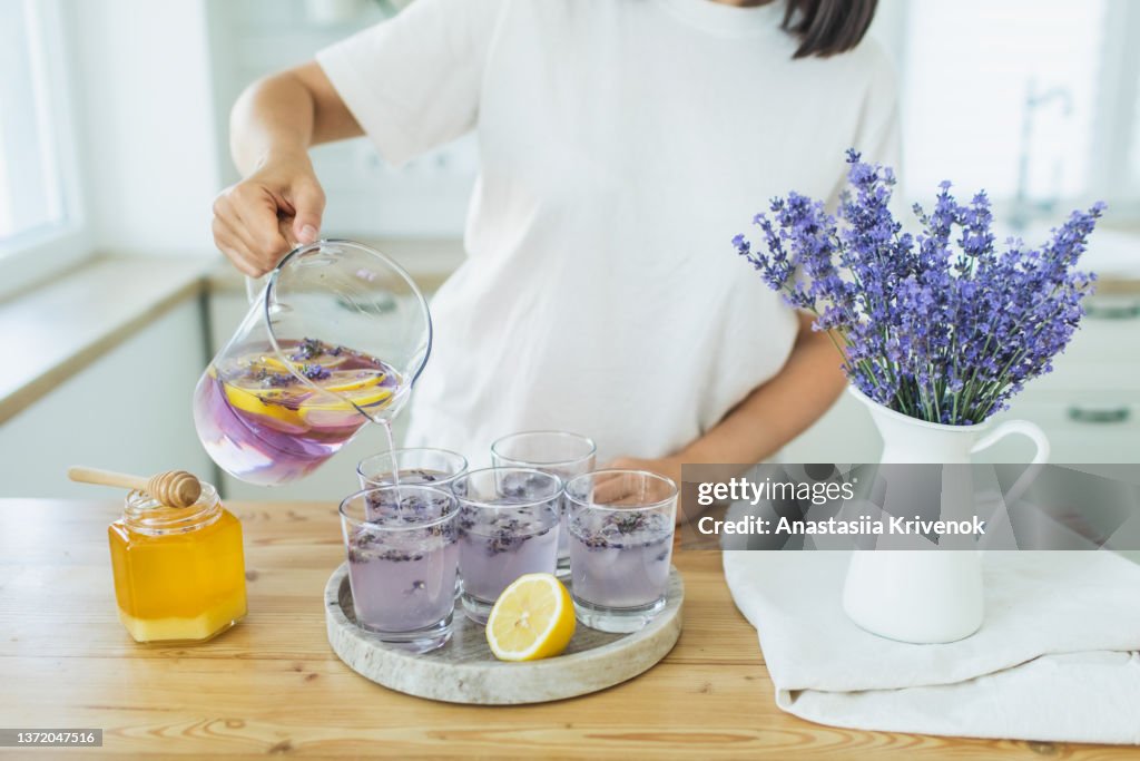 Honey, glasses with ice, lemon juice and lavender cocktail on kitchen table.