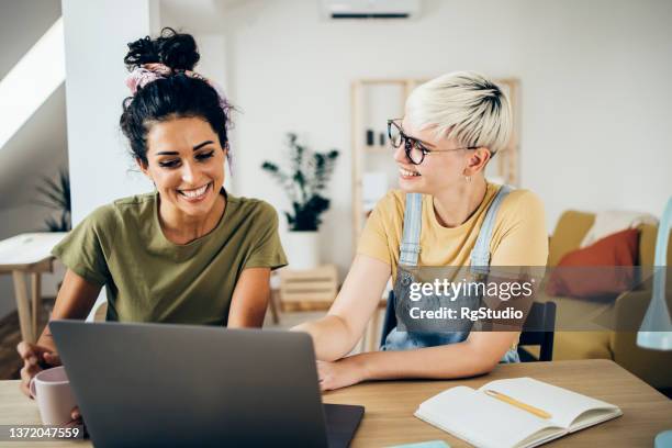 two best friends having fun while surfing the net on a laptop - flatmate stock pictures, royalty-free photos & images