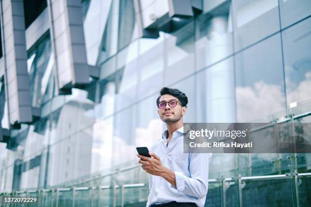 portrait of an asian young man using mobile phone on city street - asian businessman phone stockfoto's en -beelden