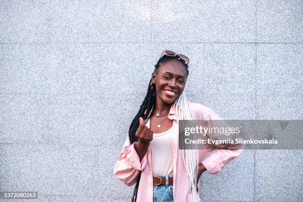 young black braided woman smiling and making heart shape by fingers outdoors. - alleen één jonge vrouw stockfoto's en -beelden