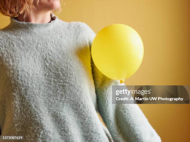 adult female (40-45 years old) wearing a wool sweater with a yellow balloon attached to it due to static electricity from the clothing. static cling concepts. - yellow perch stock-fotos und bilder