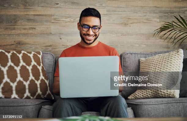 aufnahme eines gutaussehenden jungen mannes, der allein in seinem wohnzimmer sitzt und seinen laptop benutzt - reading laptop pleased stock-fotos und bilder