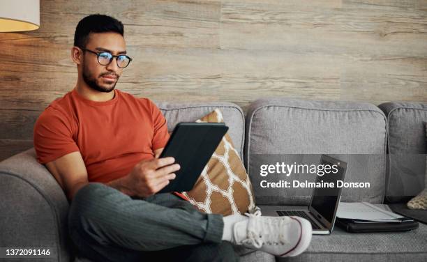 shot of a handsome young man sitting alone in his living room and using a digital tablet - blogging bildbanksfoton och bilder