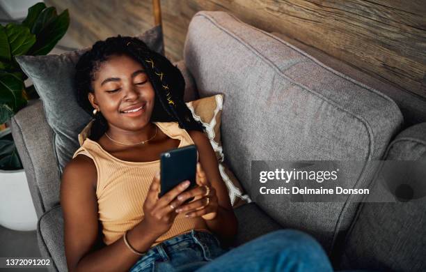 high angle shot of an attractive young woman lying on her sofa at home and using her cellphone - africa game stock pictures, royalty-free photos & images