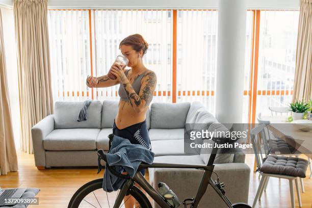 woman checking her smartwatch after a hard workout on her indoors cycling turbo trainer - protein drink stock pictures, royalty-free photos & images