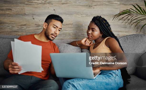 shot of a young couple sitting in the living room at home and using a laptop to calculate their finances - contemplation couple stock pictures, royalty-free photos & images