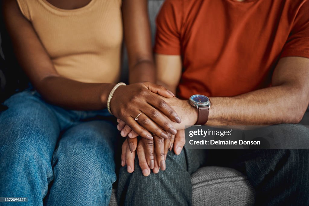 Cropped shot of an unrecognisable couple sitting together on the sofa at home and holding hands