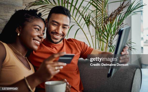 shot of a young couple sitting together in the living room and using a digital tablet for online shopping - internetbankieren stockfoto's en -beelden