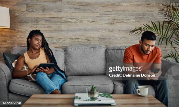 shot of a handsome young man sitting and using technology in the living room while his boyfriend watches him - suspicion stock pictures, royalty-free photos & images