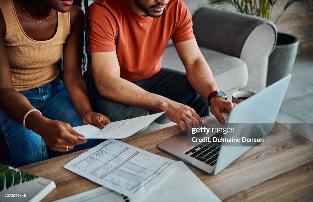 Cropped shot of an unrecognisable couple sitting in the living room and using a laptop to calculate their finances