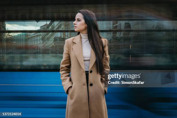 beautiful young woman against moving tram with hands in pockets - zagreb tram stock pictures, royalty-free photos & images