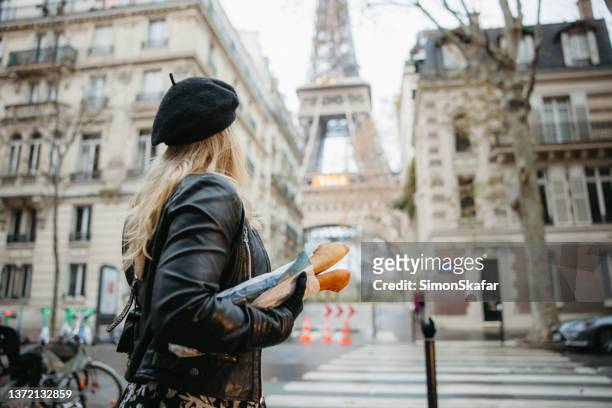 femme aux cheveux blonds, debout à un passage pour piétons, portant deux baguettes, tour eiffel, paris en arrière-plan - french bakery photos et images de collection