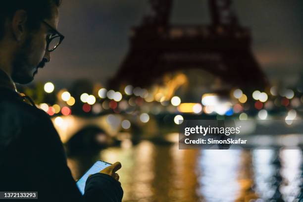 nahaufnahme eines mannes, der abends vor dem eiffelturm in paris auf sein smartphone blickt - brille fluss stadt stock-fotos und bilder